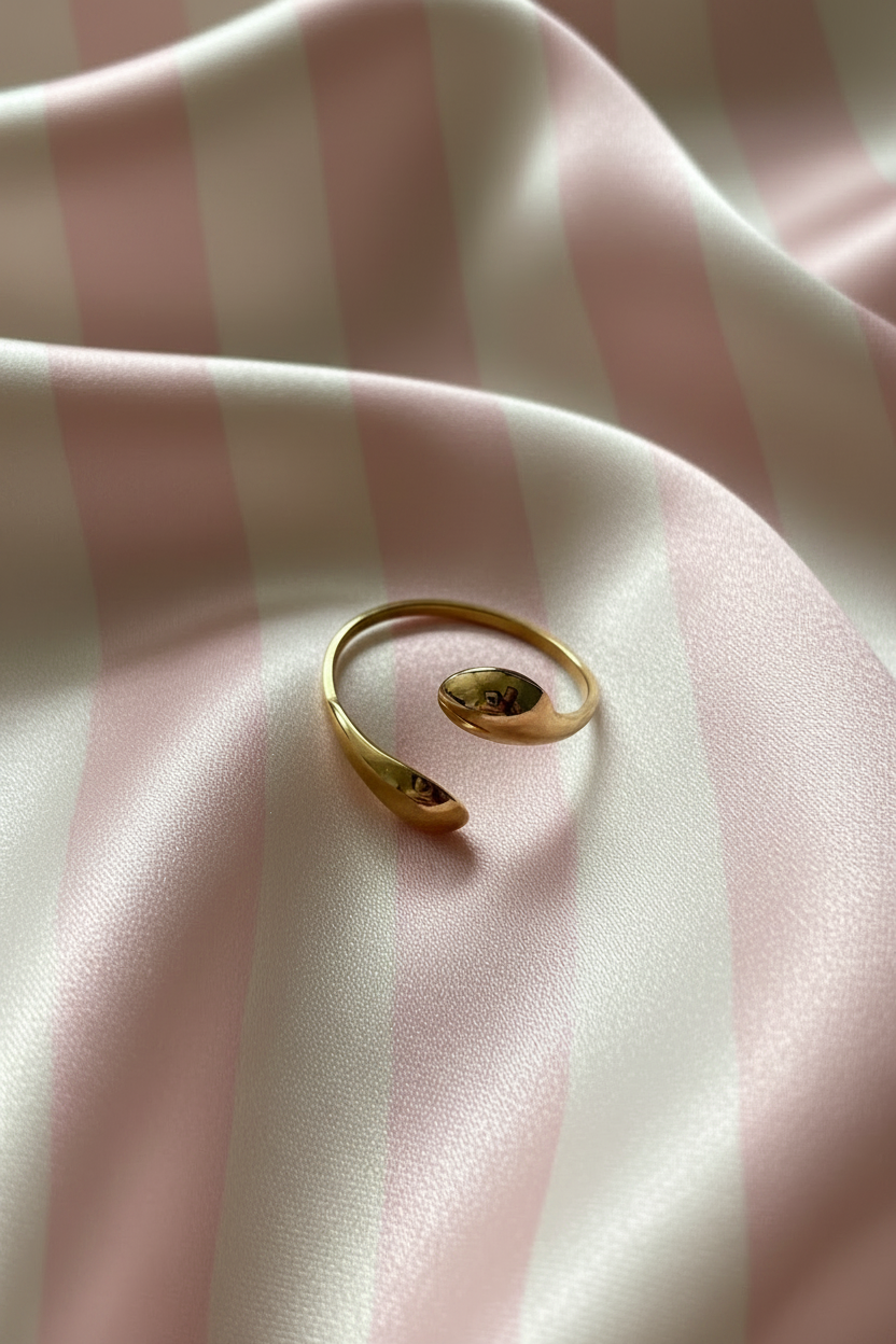 Bague bypass gouttes dorées vue de dessus sur rayures rose poudre et crème satiné