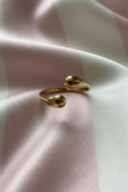 Bague bypass gouttes dorées vue de face sur rayures rose poudre et crème satiné