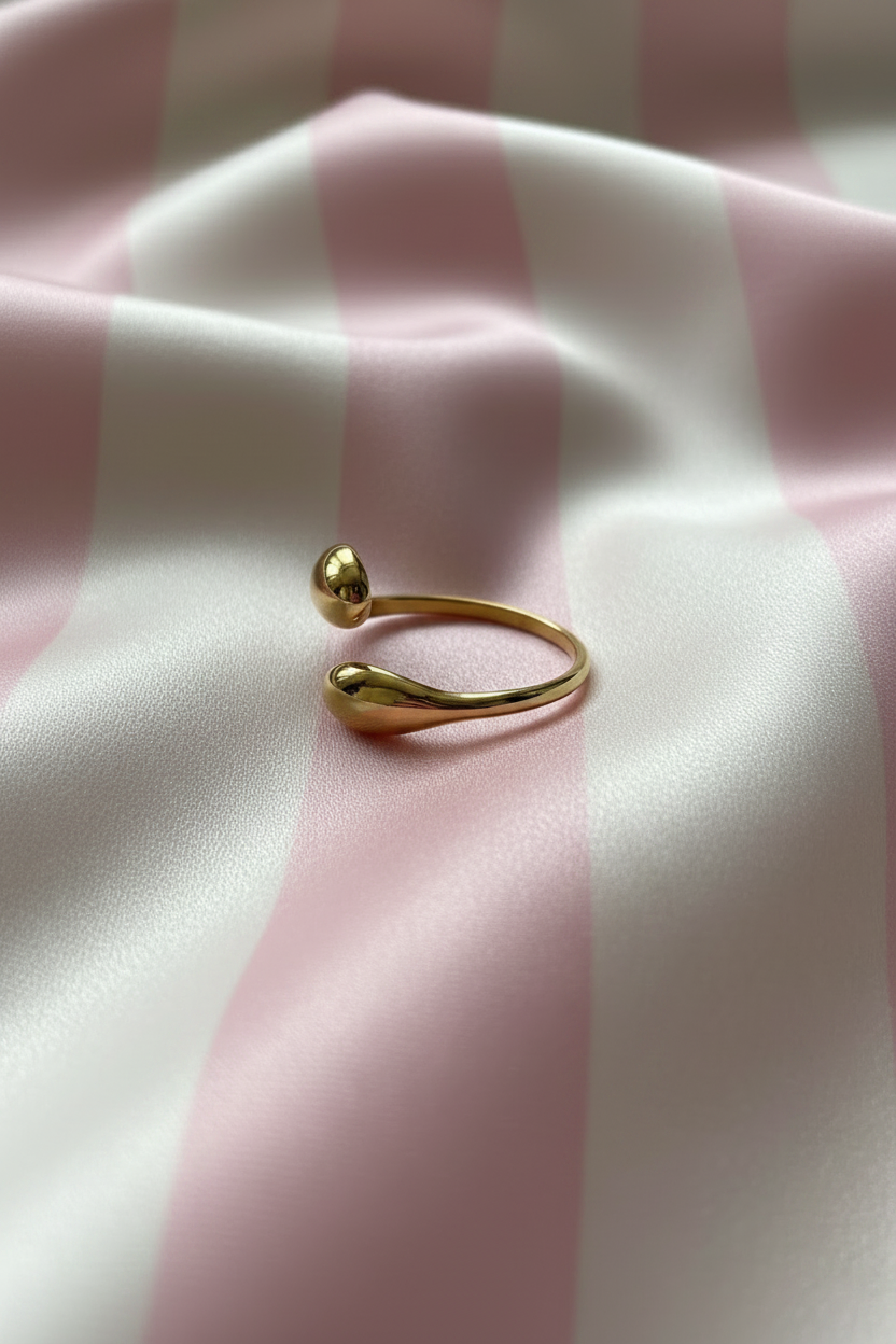 Bague bypass gouttes dorées vue en angle sur rayures rose poudre et crème satiné