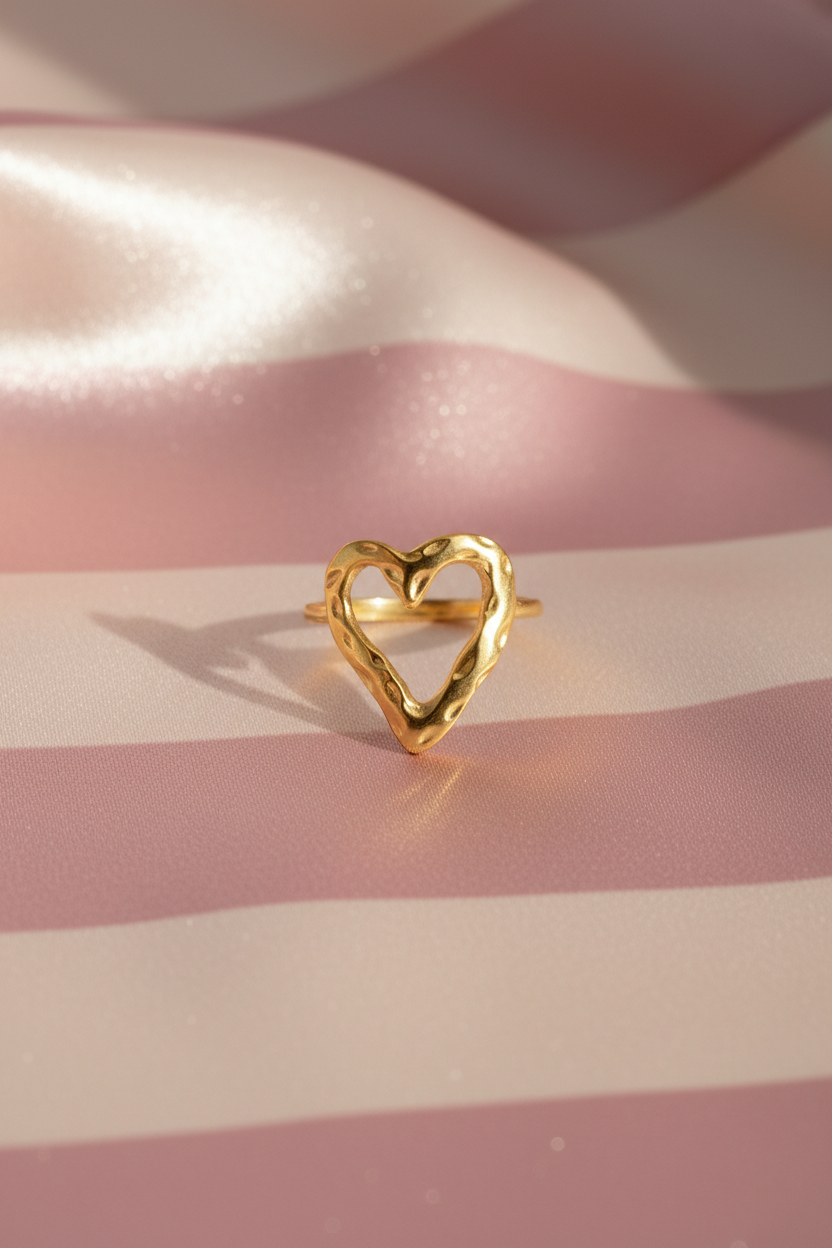 Bague cœur dorée fondu vue de face sur rayures rose poudre et crème satiné