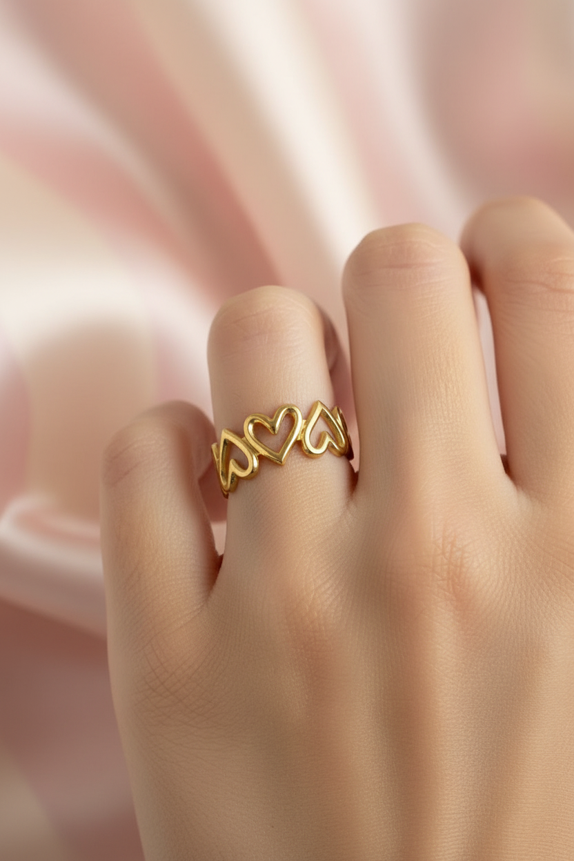 Bague couronne cœurs dorée portée sur main sur fond rayures rose poudre et crème satiné