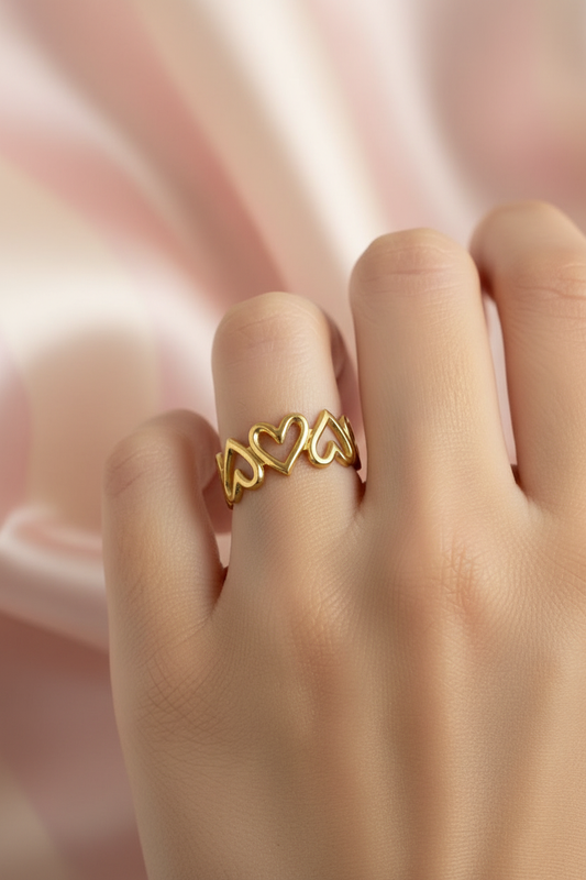 Bague couronne cœurs dorée portée sur main sur fond rayures rose poudre et crème satiné