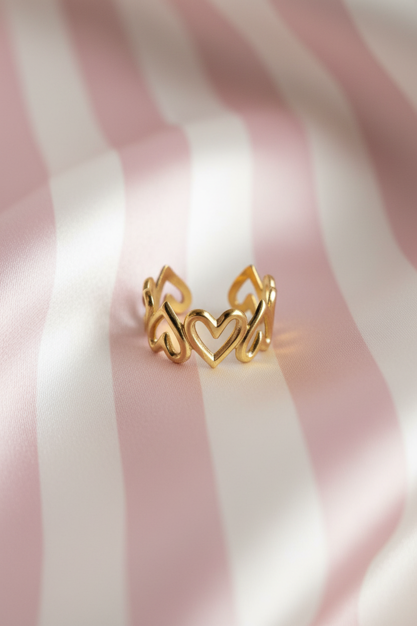 Bague couronne cœurs dorée vue de face sur rayures rose poudre et crème satiné