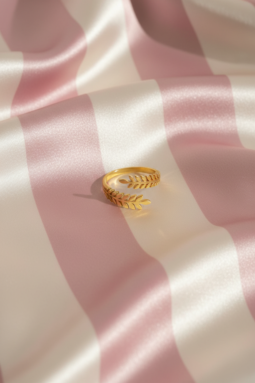 Bague feuilles dorée vue de dessus sur rayures rose poudre et crème satiné