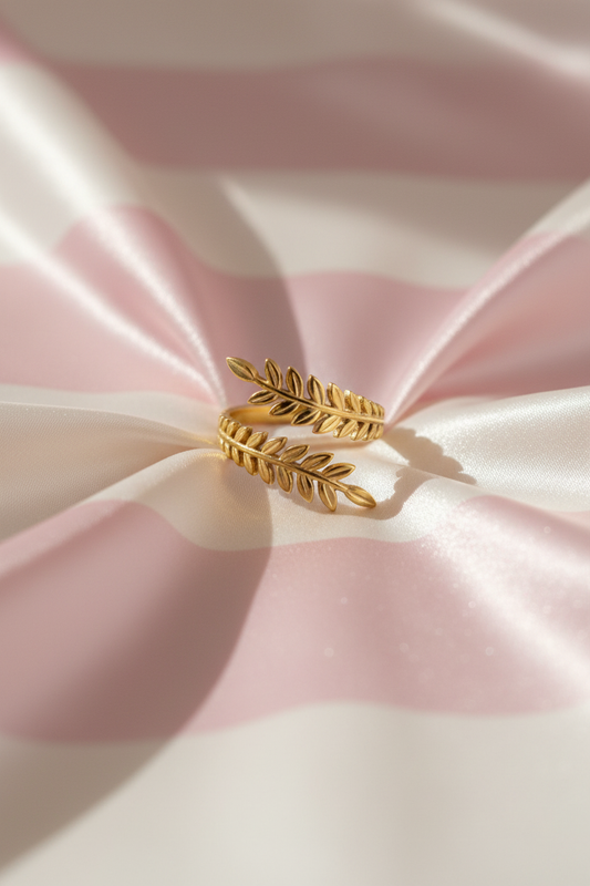 Bague feuilles dorée vue de face sur rayures rose poudre et crème satiné