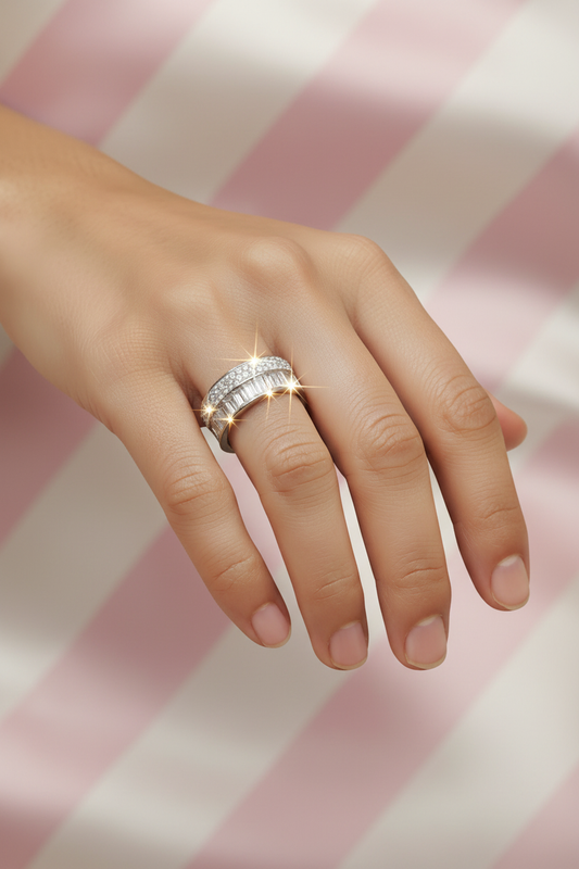 Bague large diamants baguettes argentée portée sur main sur fond rayures rose poudre et crème satiné