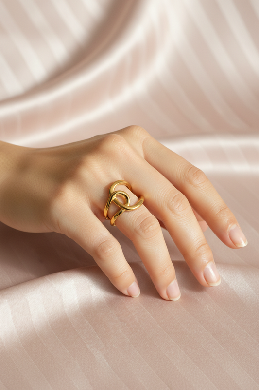 Bague nœud dorée portée sur fond satin rose poudre rayé