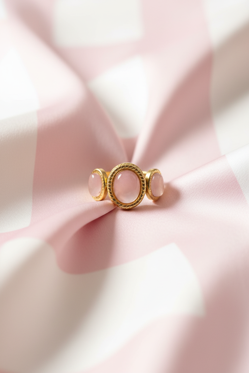 Bague trio pierres roses dorée vue de face sur rayures rose poudre et crème satiné